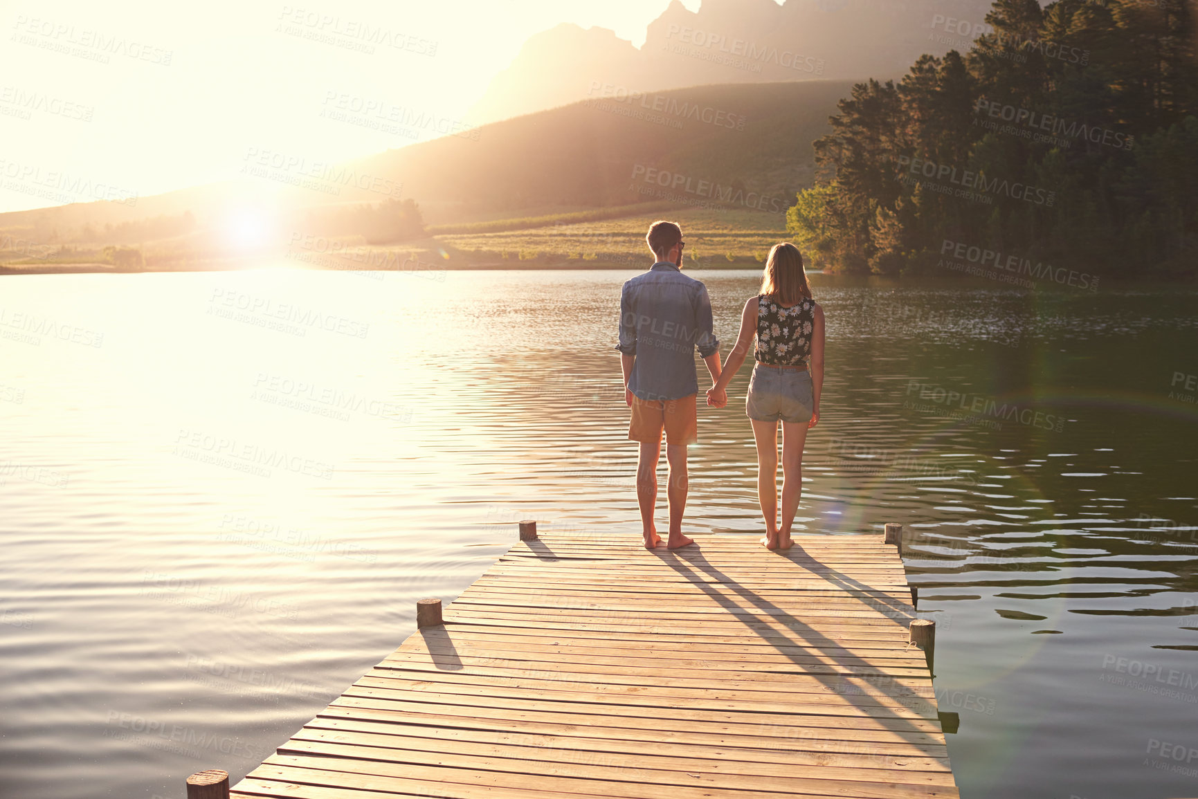 Buy stock photo Couple, holding hands and sunset on dock by lake for memory, vacation and love in countryside. People, man and woman with back, water and view in nature with bonding, relationship and holiday in USA