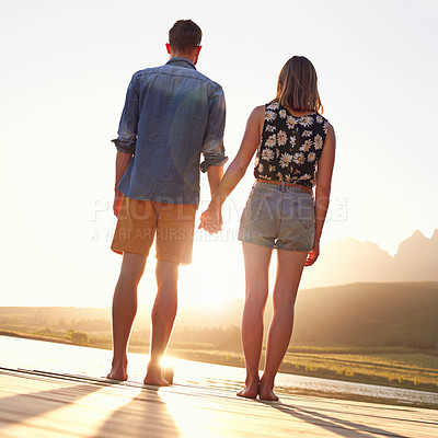Buy stock photo Rearview shot of an affectionate young couple standing on a dock at sunset