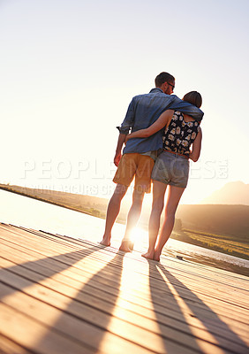 Buy stock photo Rearview shot of an affectionate young couple standing on a dock at sunset