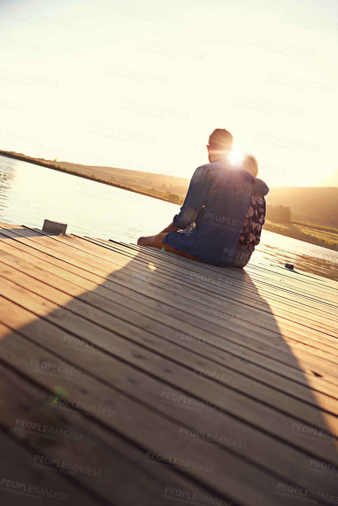 Buy stock photo Couple, hug and sunset on pier by lake for memory, vacation or love in countryside. People, man and woman with back, water and embrace for view in summer with care, relationship or holiday in Italy