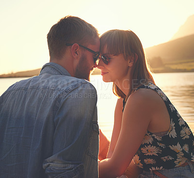 Buy stock photo Shot of an affectionate young couple sitting on a dock at sunset