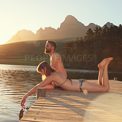 Buy stock photo Shot of an affectionate young couple in swimsuits sitting on a dock at sunset