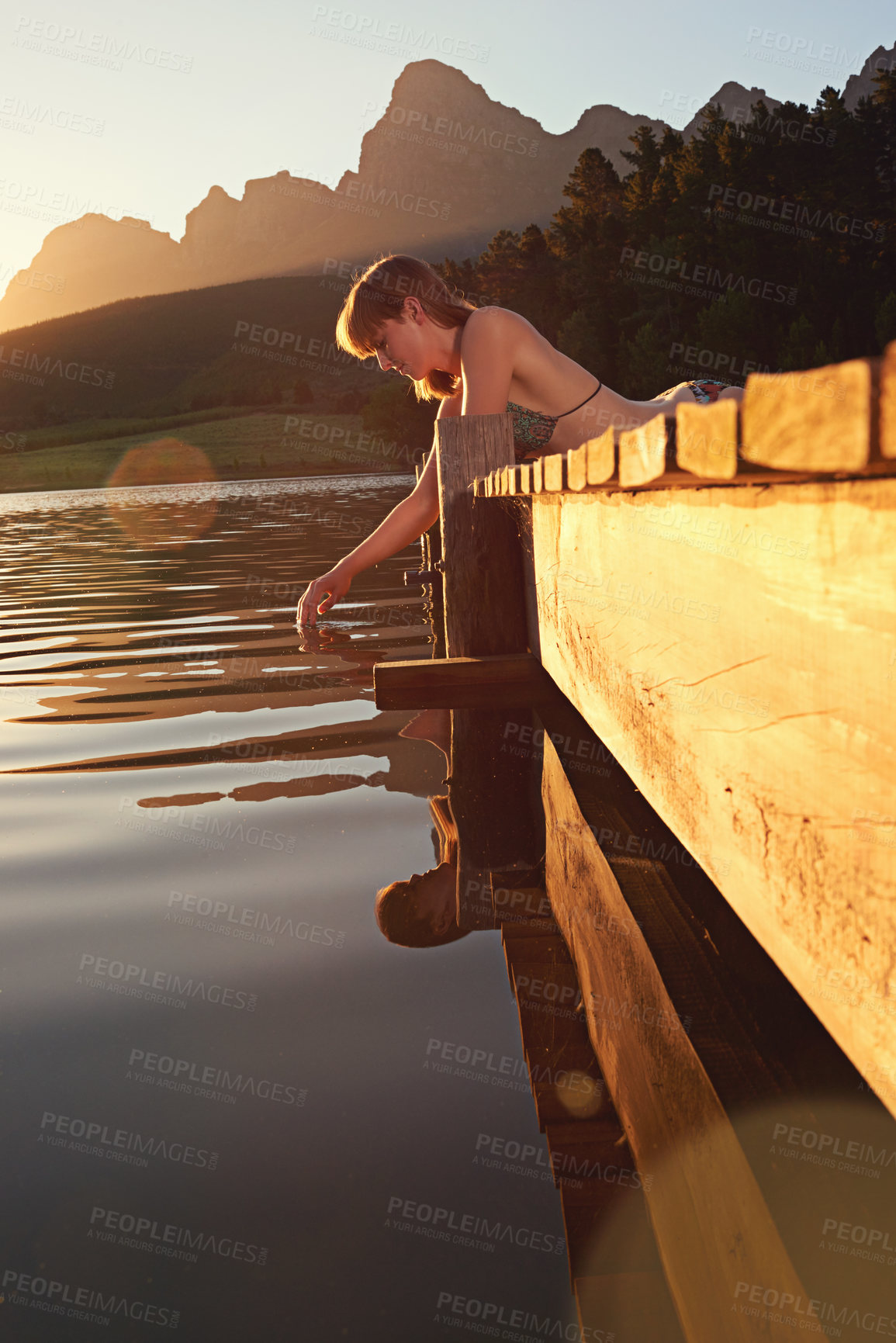 Buy stock photo Woman, lake and playing with water on pier for summer holiday, travel adventure or relax in bikini. Sunset, girl and person by river in countryside for sensory experience, natural connection or break