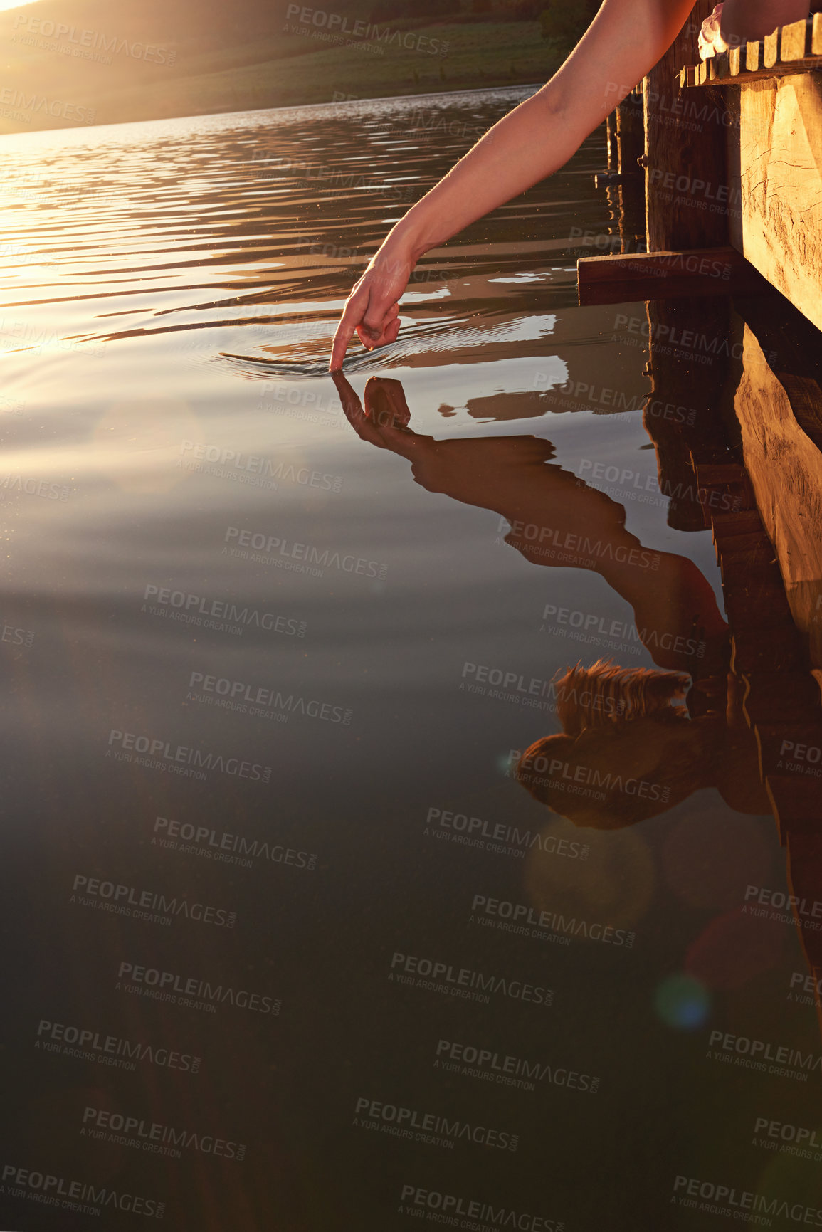 Buy stock photo Shot of a young woman lying on a dock touching the water