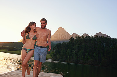 Buy stock photo Shot of an affectionate young couple in swimsuits walking on a dock at sunset