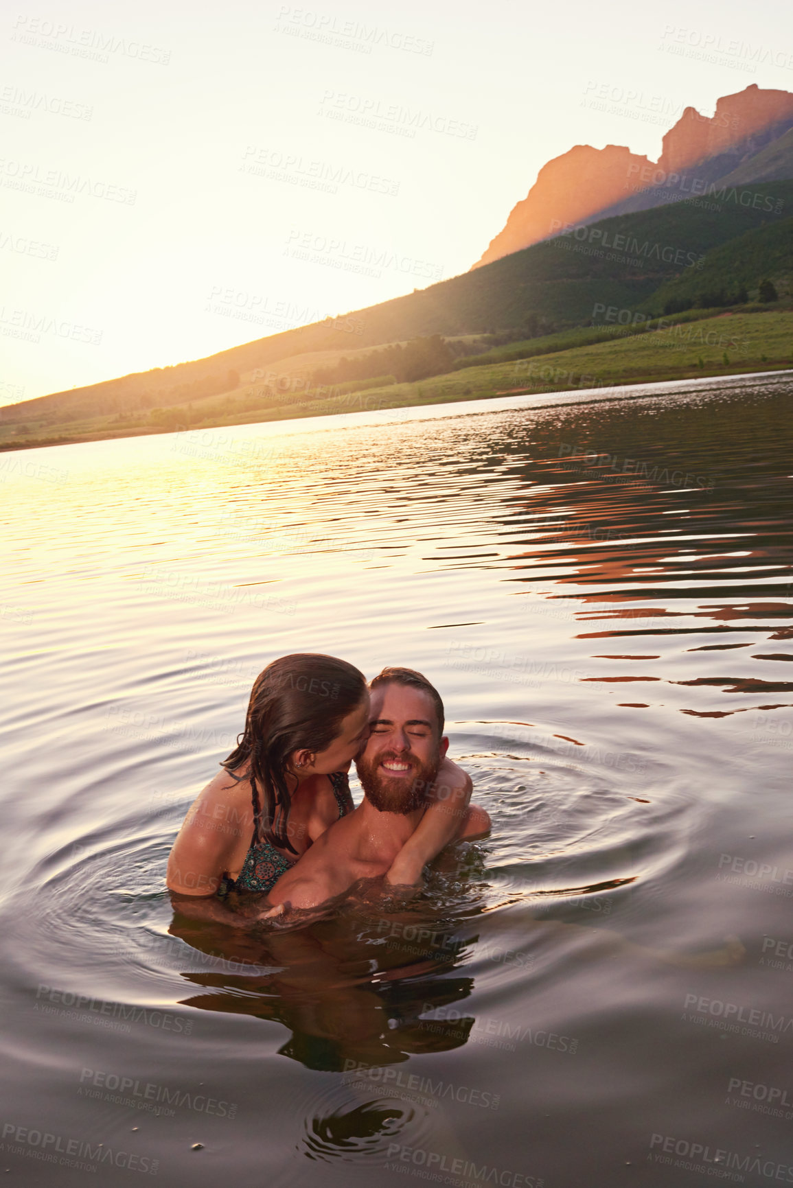 Buy stock photo Swimming, sunset and couple hug at lake together on vacation, romantic anniversary or holiday. Relationship, support and people kiss in water for bonding, love or trust on honeymoon date for travel