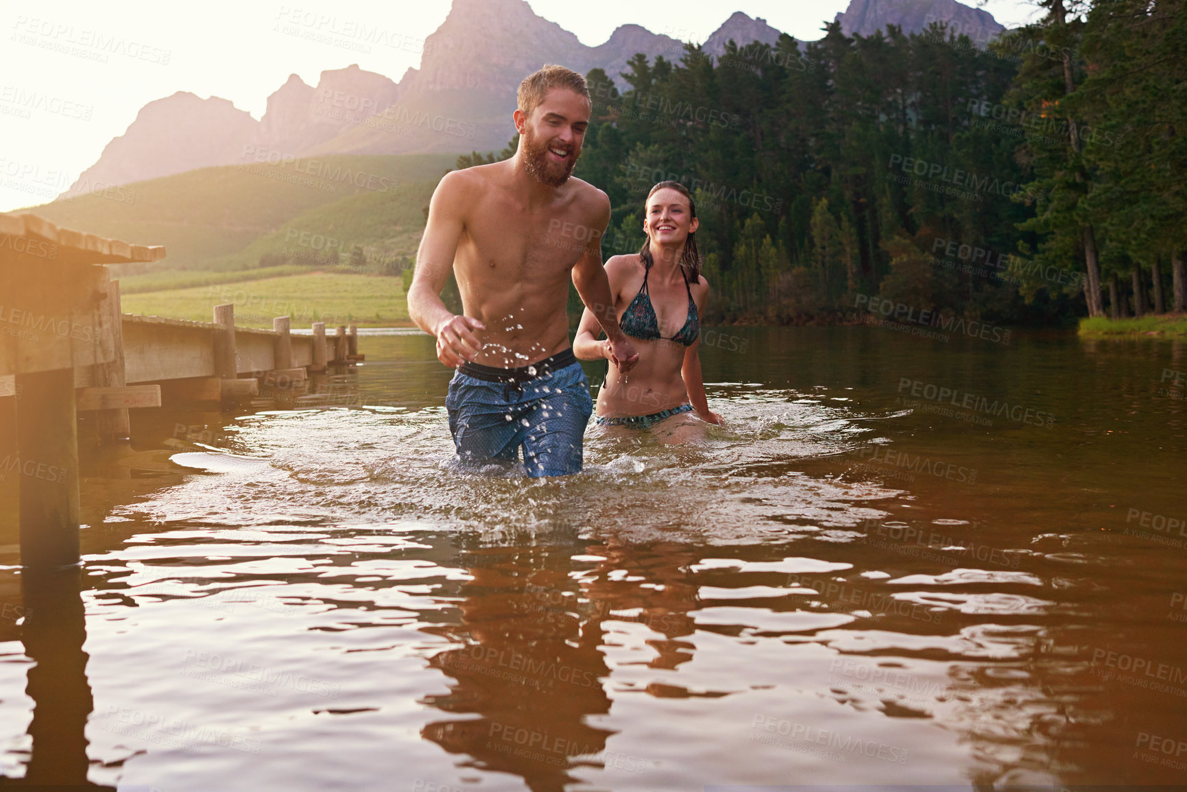 Buy stock photo Swimming, happy and couple at lake laughing together on vacation, romantic anniversary or holiday. Holding hands, playing and people splash in water for bonding, love or trust on honeymoon for travel