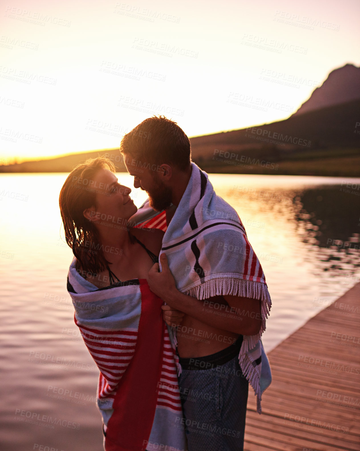 Buy stock photo Hug, sunset or couple with towel at lake together on vacation, anniversary and outdoor holiday. Relationship, relax or happy people on dock for bonding, swimming and love on romantic honeymoon date