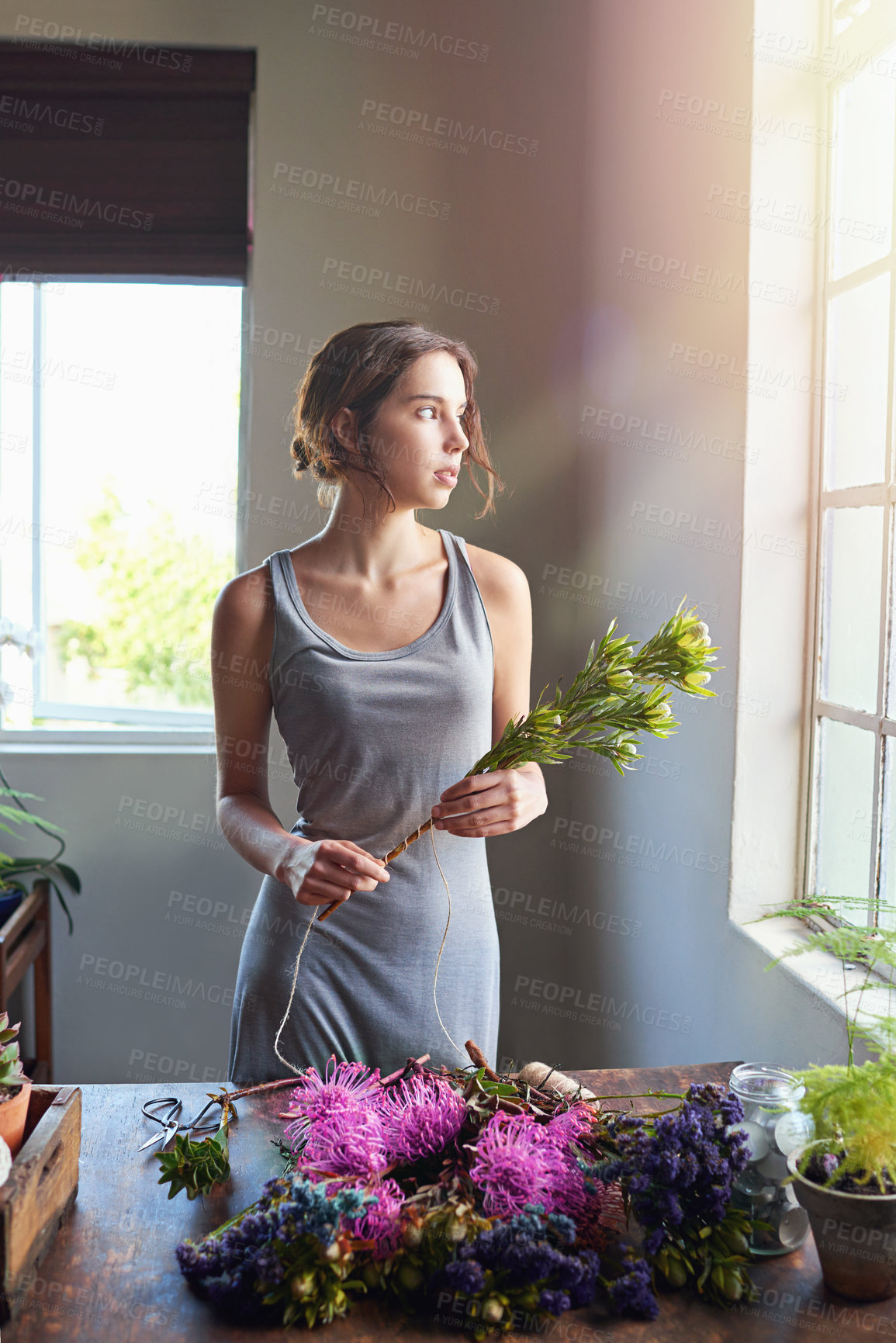 Buy stock photo Shot of a beautiful woman completing a floral bouquet on a wooden counter top