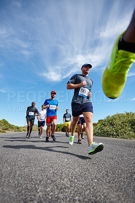 Buy stock photo Low angle shot of a group of young men running a marathon