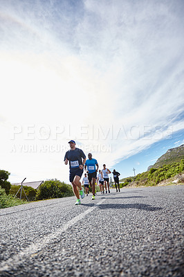 Buy stock photo Low angle shot of a group of young men running a marathon