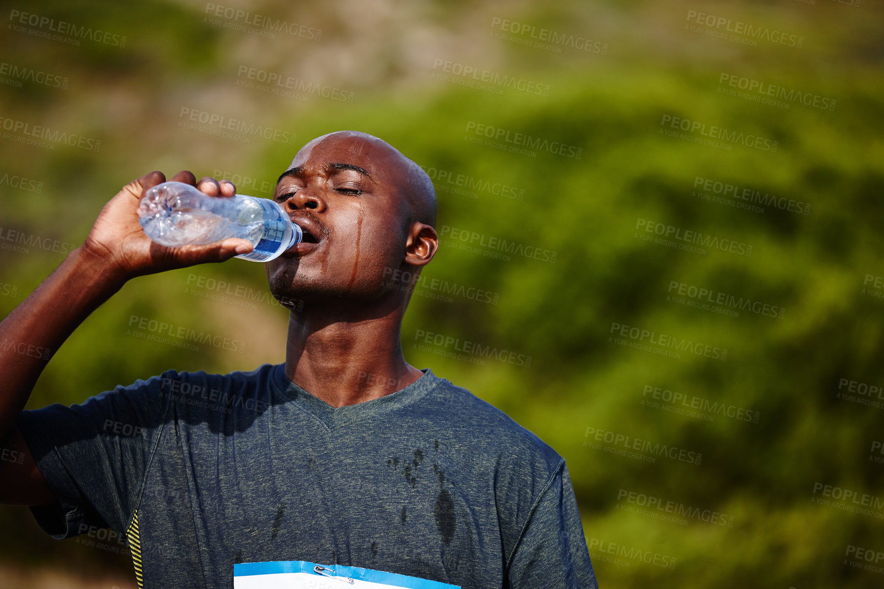 Buy stock photo Shot of a young male runner drinking from his water bottle during a race