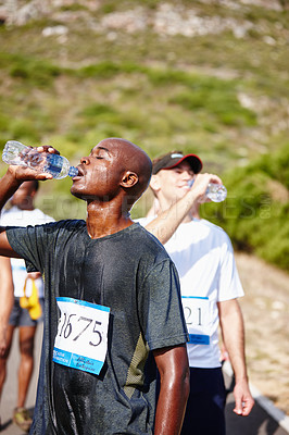 Buy stock photo Shot of a group of young runners catching their breath and drinking water after a race