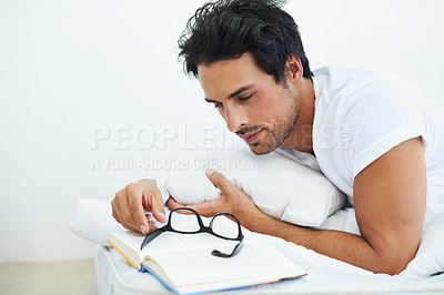 Buy stock photo Relax, bedroom and man reading a book with glasses for knowledge on a weekend morning in his home. Education, study or learning with a casual young person lying on a bed for a hobby in his apartment