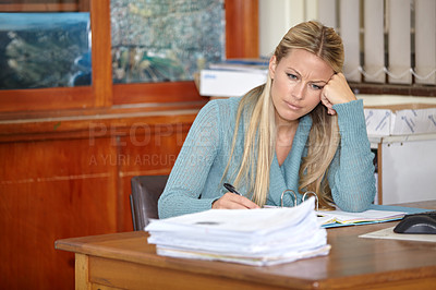 Buy stock photo A tired young teacher sitting at her classroom desk marking classwork and tests
