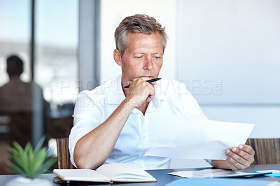 Buy stock photo Shot of a handsome businessman going through his paperwork in the office
