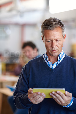 Buy stock photo Shot of a handsome businessman using a digital tablet in a casual office