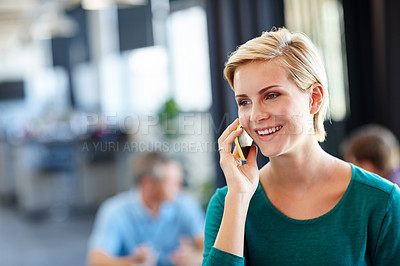Buy stock photo Shot of an attractive woman using her cellphone with her colleagues blurred in the background