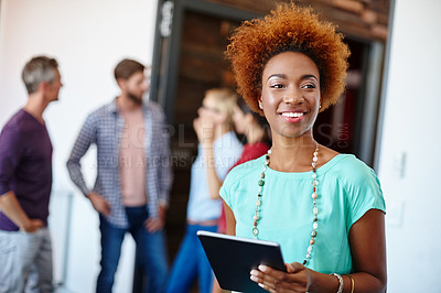 Buy stock photo Shot of a young designer using a tablet with her colleagues standing in the background