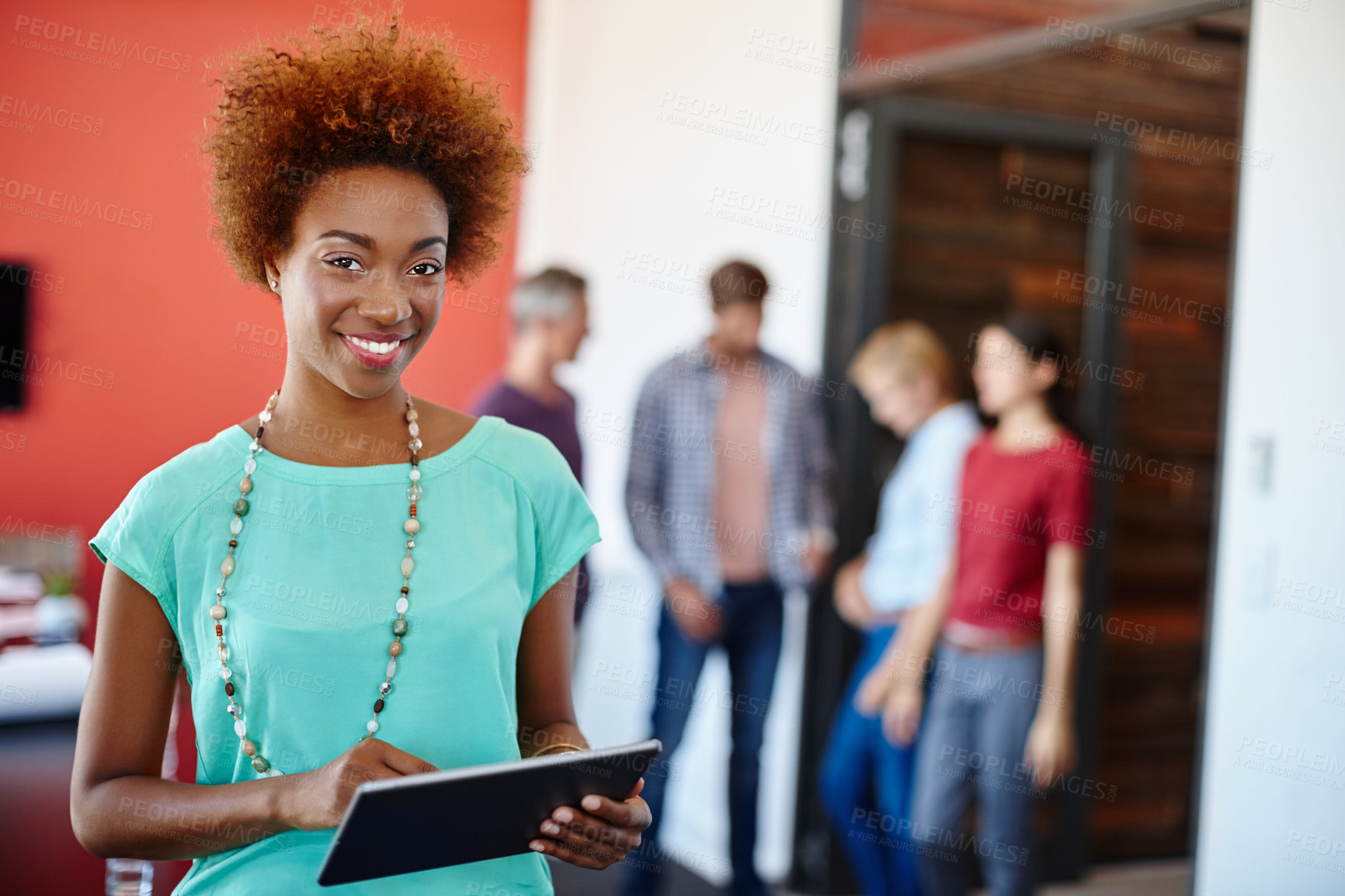 Buy stock photo Shot of a young designer using a tablet with her colleagues standing in the background