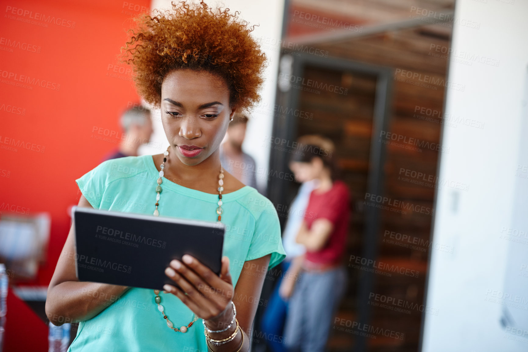 Buy stock photo Shot of a young designer using a tablet with her colleagues standing in the background