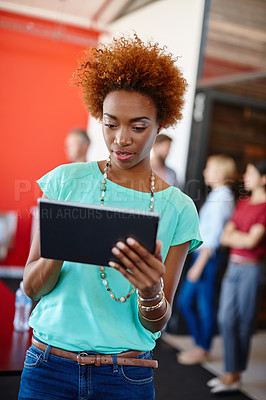 Buy stock photo Shot of a young designer using a tablet with her colleagues standing in the background