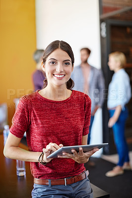 Buy stock photo Shot of a young designer using a tablet with her colleagues standing in the background