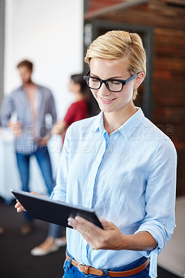 Buy stock photo Shot of a young designer using a tablet with her colleagues standing in the background