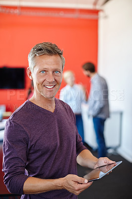 Buy stock photo Shot of a handsome designer using a tablet with his coworkers in the background