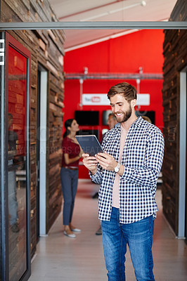 Buy stock photo Shot of a young designer using a tablet with her colleagues standing in the background