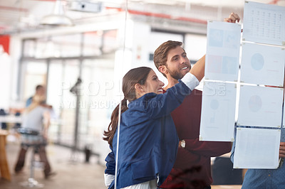 Buy stock photo Cropped shot of two creative professionals working together at a glass wall with designs on it