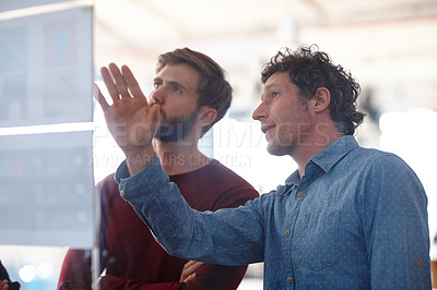 Buy stock photo Two creative professionals working together at a glass wall with designs on it