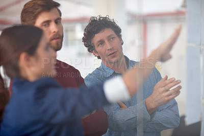 Buy stock photo A group of creative professionals working together at a glass wall with designs on it