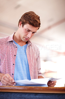 Buy stock photo Cropped shot of a handsome young businessman looking over some paperwork