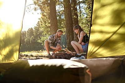 Buy stock photo Shot of a young couple starting a fire by hand while camping