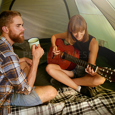 Buy stock photo Shot of a young woman playing guitar to her boyfriend in a tent