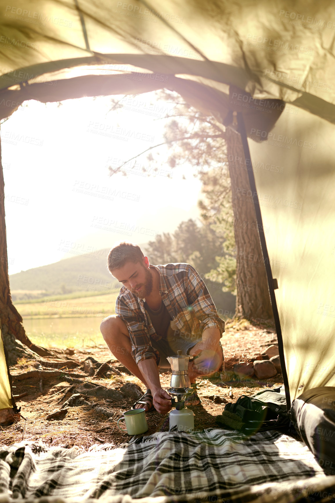 Buy stock photo Shot of a young man making coffee on a camp stove while camping