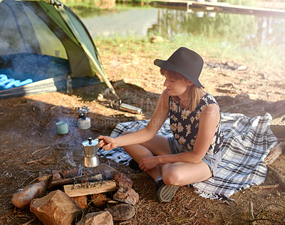 Buy stock photo Shot of a young woman making coffee over an open fire at a campsite