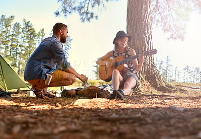 Buy stock photo Shot of a young woman playing guitar for her boyfriend at their campsit