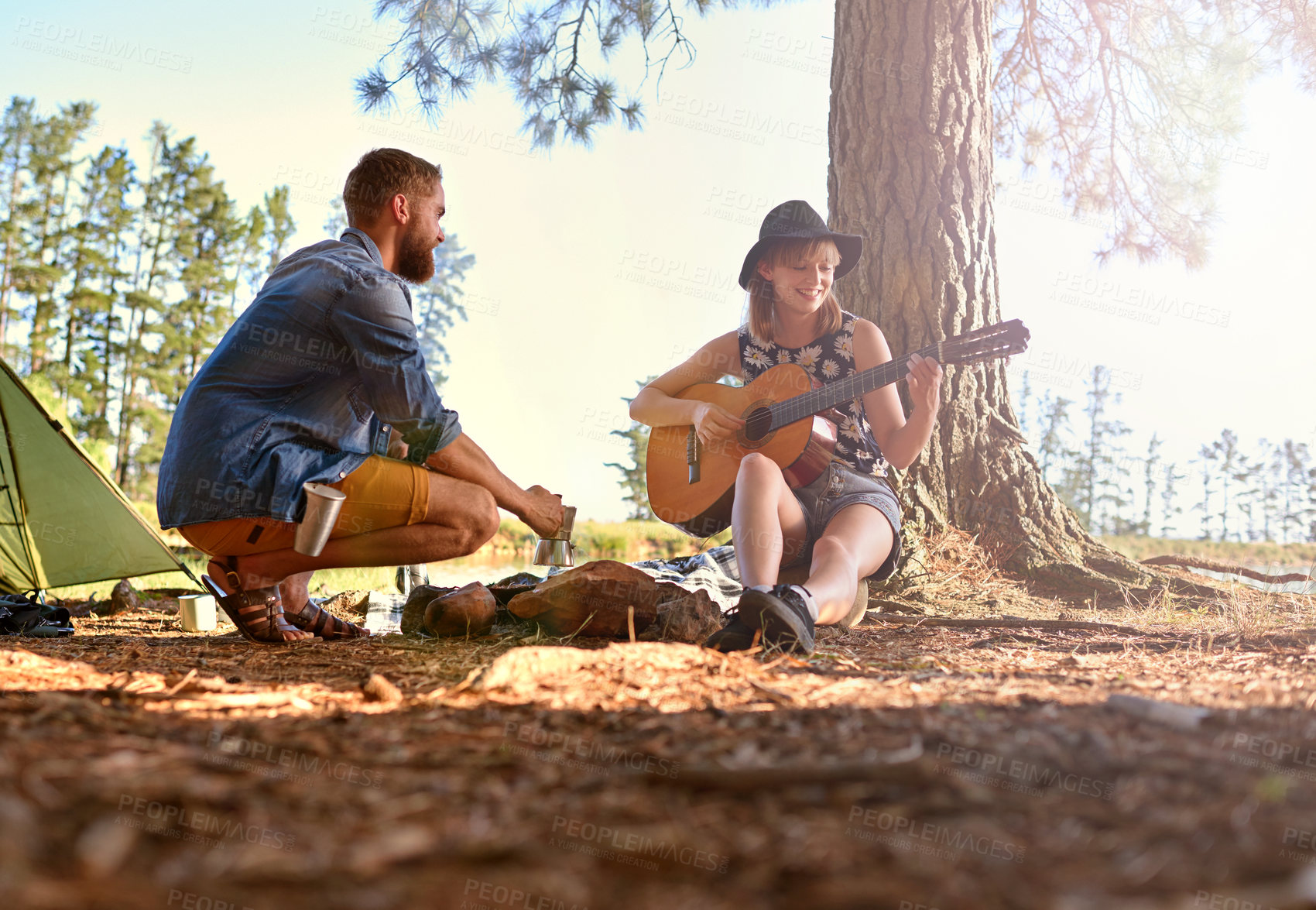 Buy stock photo Shot of a young woman playing guitar for her boyfriend at their campsit