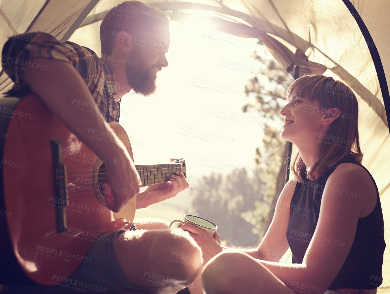 Buy stock photo Shot of a young man playing guitar to his girlfriend in a tent