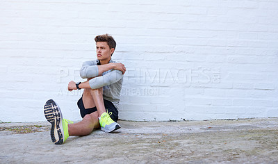 Buy stock photo Shot of a sporty young man stretching his legs before exercising