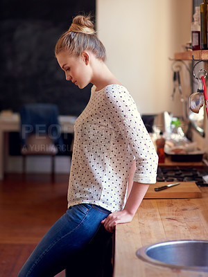 Buy stock photo Shot of a young woman standing leaning on the kitchen counter looking thoughtful