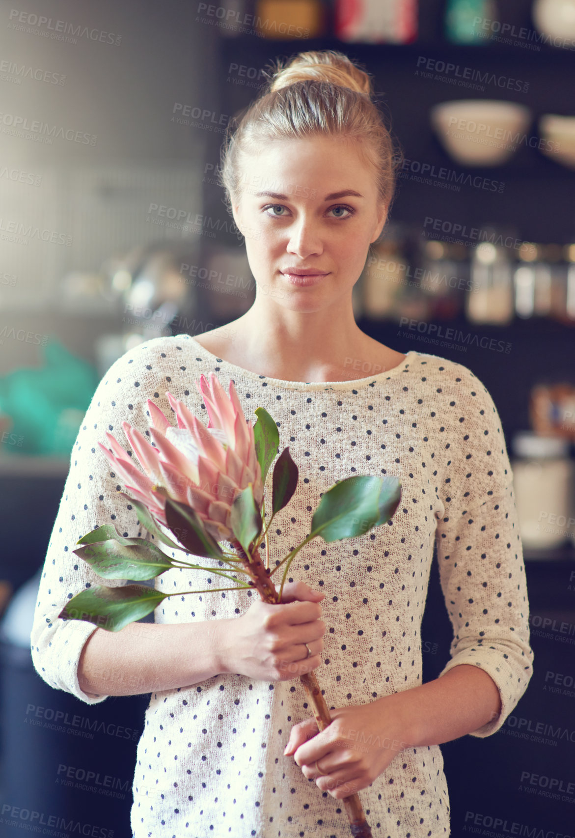 Buy stock photo Shot of a beautiful young woman standing in her kitchen holding a protea flower