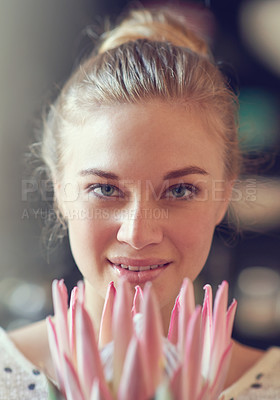 Buy stock photo Closeup portrait of a beautiful young woman holding a protea flower indoors