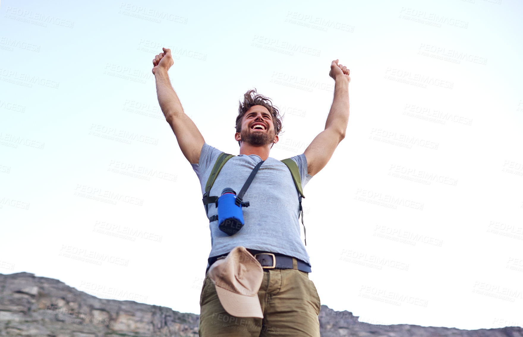 Buy stock photo Shot of a handsome young man standing with his arms raised while hiking