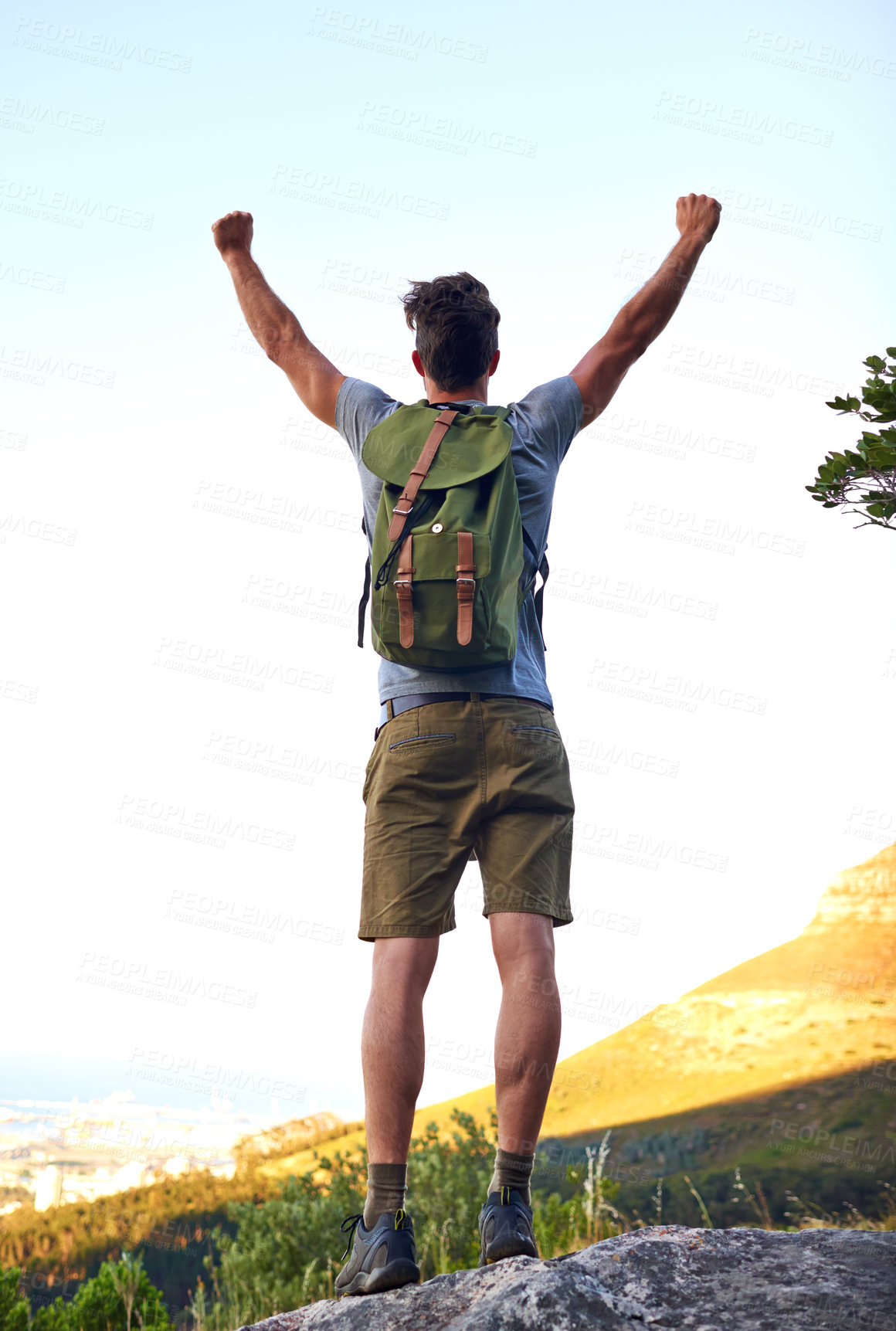 Buy stock photo Shot of a handsome young man standing with his arms raised while hiking