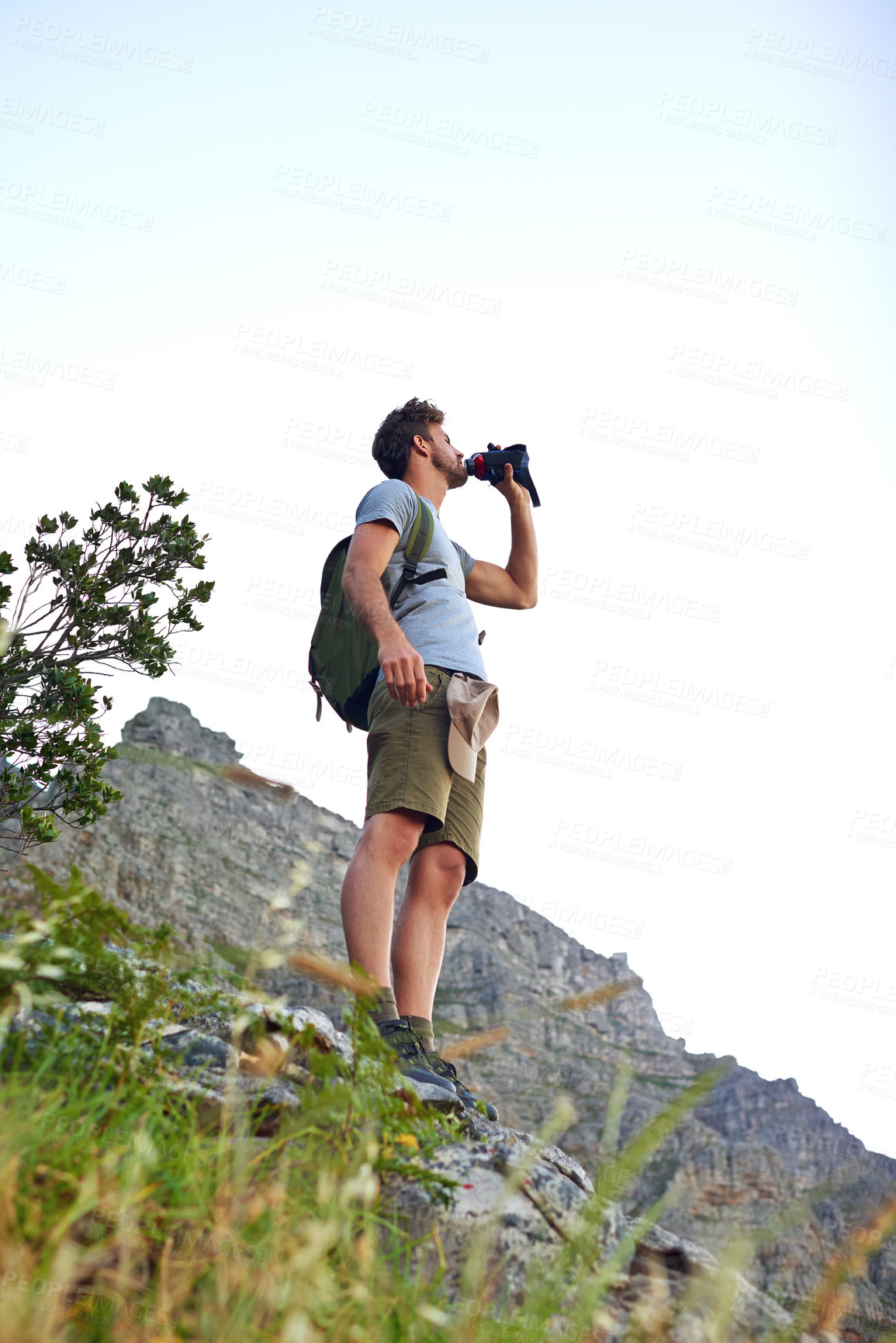 Buy stock photo Shot of a handsome young man taking a drink of water while hiking