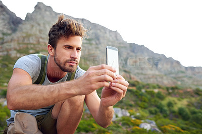 Buy stock photo Shot of a handsome young man snapping pics while hiking