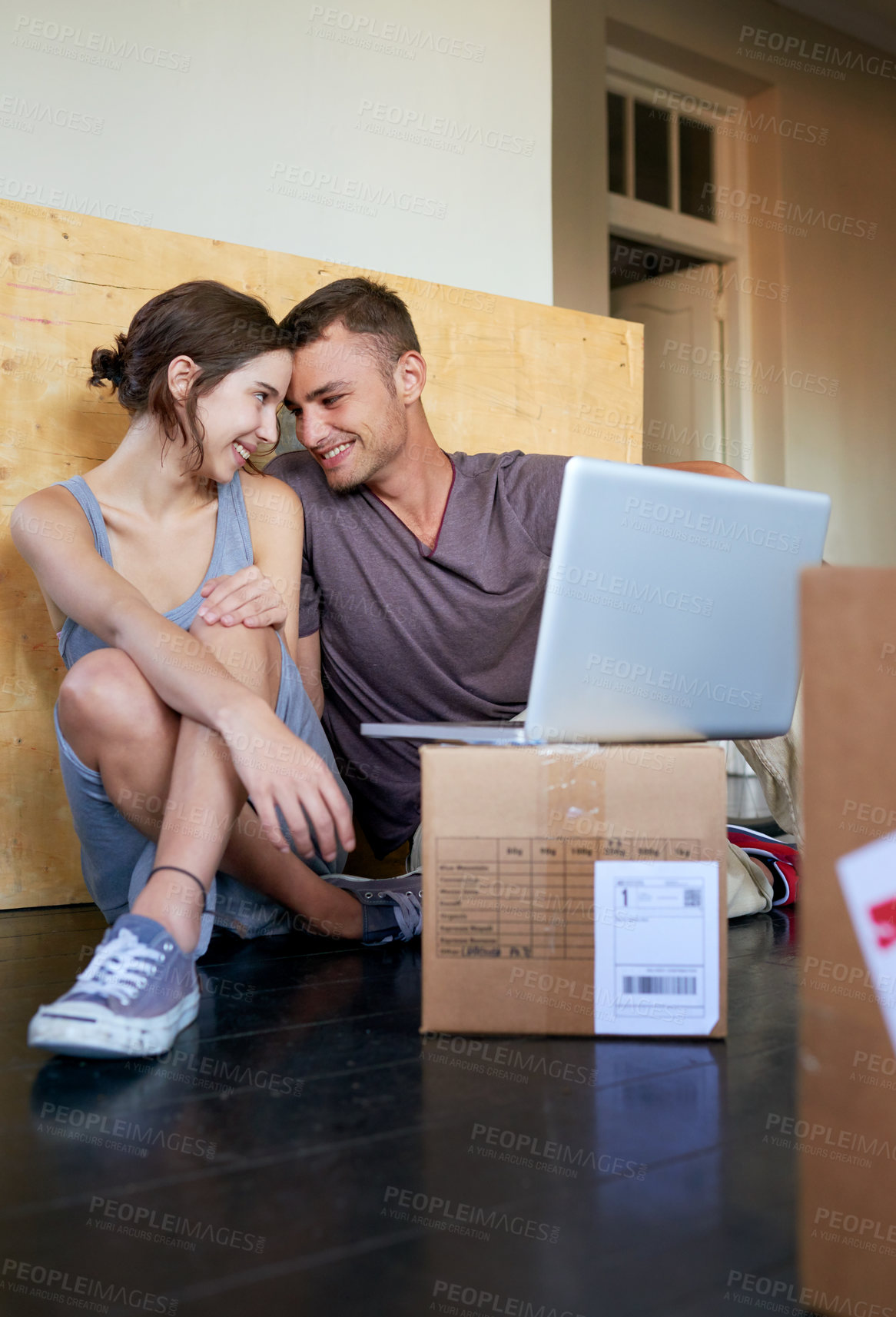 Buy stock photo Shot of an affectionate young couple using a laptop on the floor at home